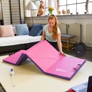 Frau faltet pinke, 5 cm dicke eyepower Gymnastikmatte (200x60 cm) für Fitnessübungen zu Hause. Ideal für Sport.