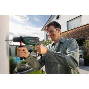 Mann bohrt mit Bosch UniversalImpact 800 Schlagbohrmaschine in Wand. Bohrmaschine in Grün/Schwarz.