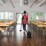 Frau saugt mit Kärcher T 11/1 Classic Trockensauger einen Klassenraum.