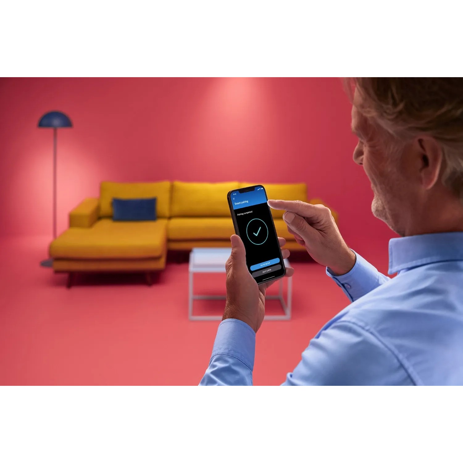 Mann steuert WIZ Deckenleuchte Imageo per App im Wohnzimmer.