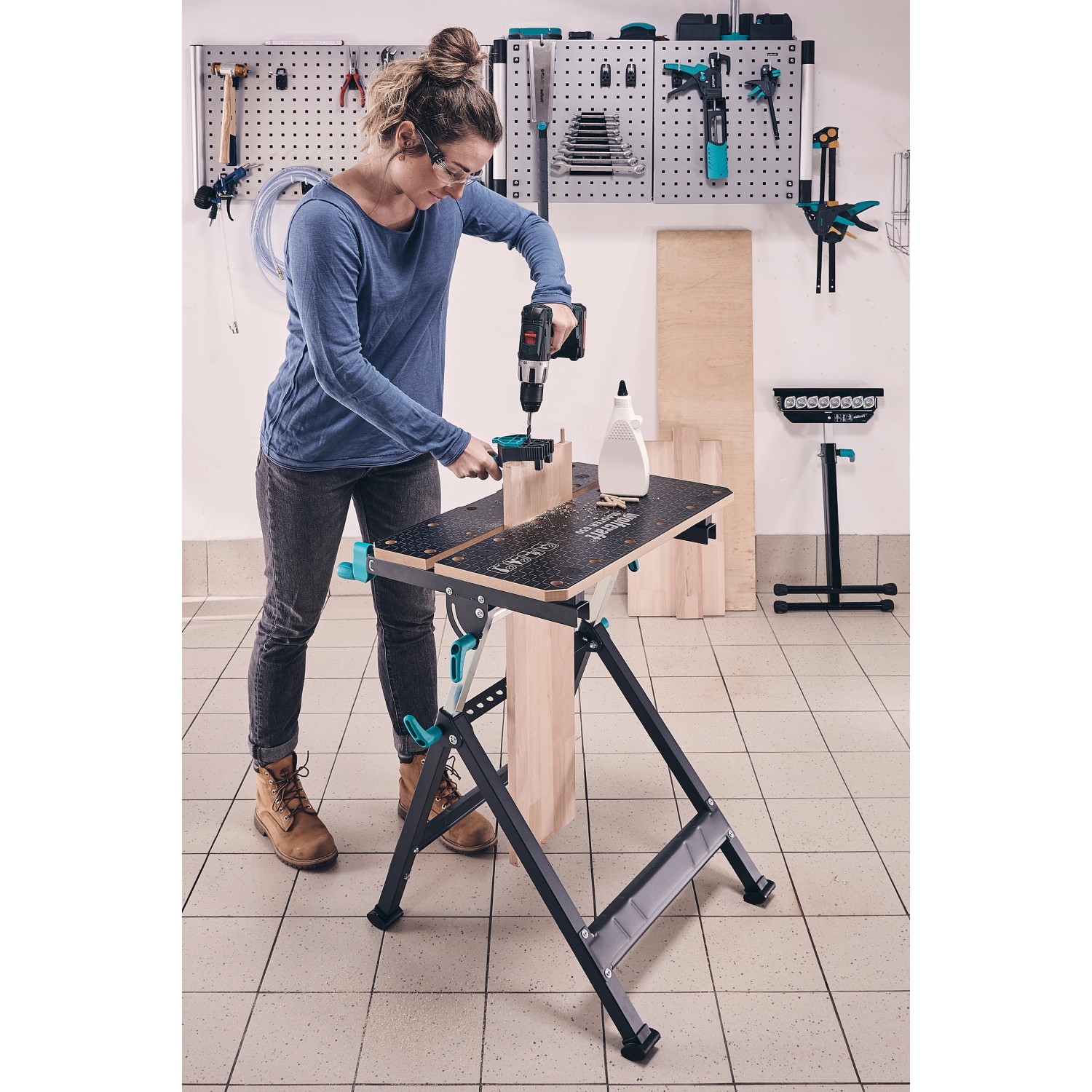 Frau bohrt Werkstück auf Wolfcraft Master 650 Ergo Werkbank. Höhenverstellbarer Spanntisch mit Stahlrohrgestell.