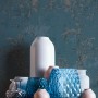 Blaue Vliestapete mit Barockmuster und Glanz-Effekt vor Deko-Vasen.