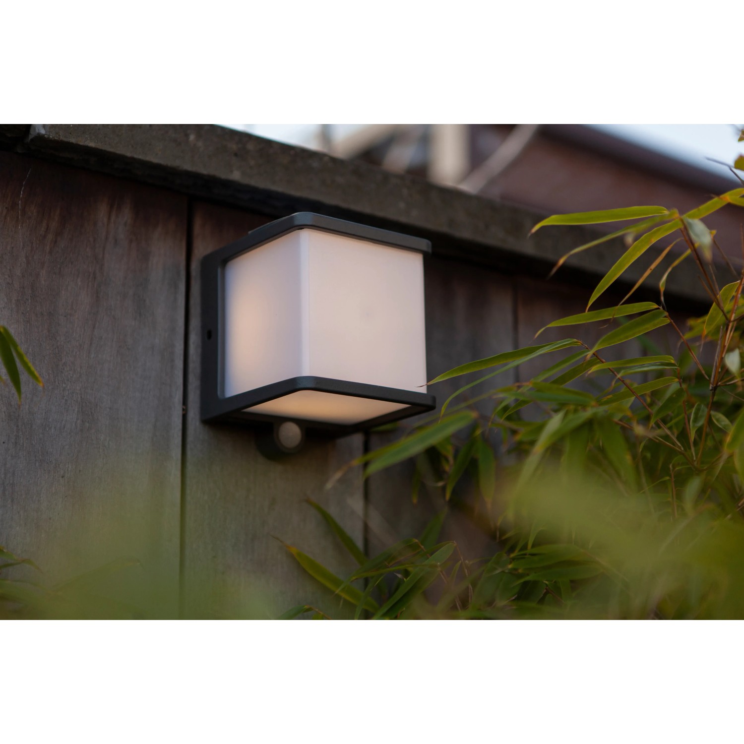 Anthrazitfarbene Lutec LED Solar Wandleuchte Doblo mit Bewegungsmelder an Holzwand.