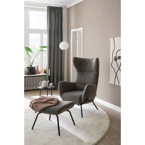 Grauer Sessel mit Hocker auf rundem Teppich in Wohnzimmer-Szene.