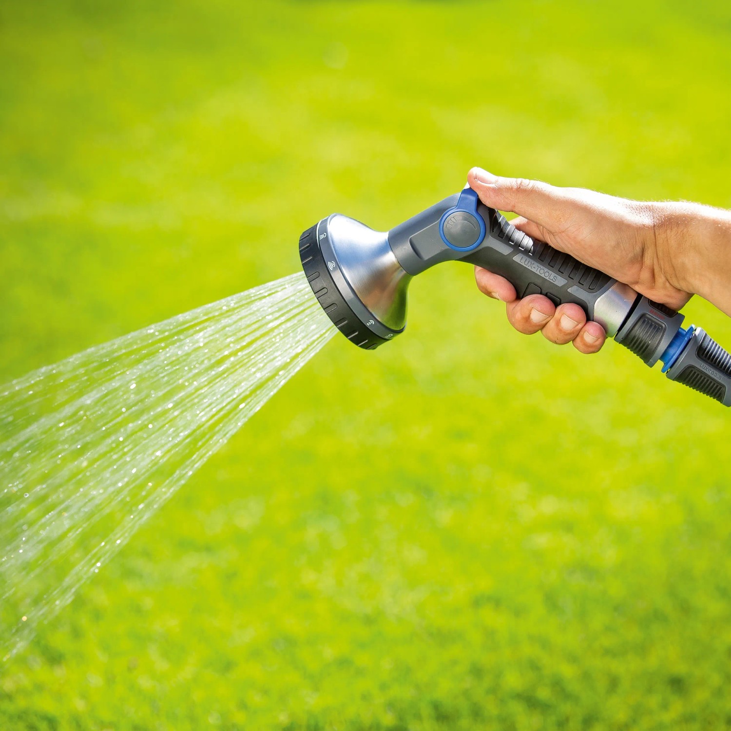 Hand hält LUX Multifunktionsbrause mit 10 Strahlvarianten beim Bewässern des Gartens.