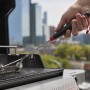 Reinigung einer Grillfläche mit einer Grillbürste. Weber Gasgrill im Hintergrund.