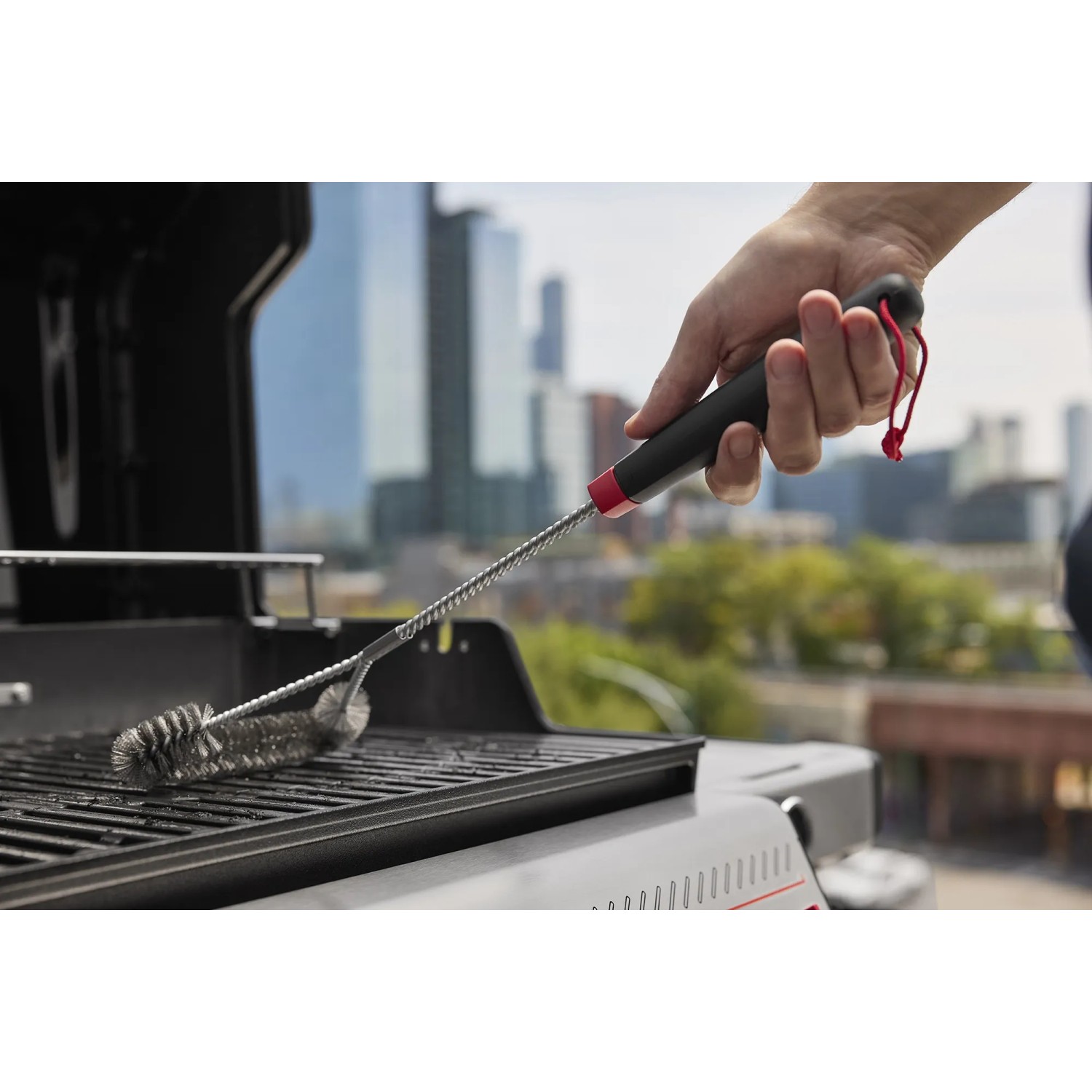 Reinigung einer Grillfläche mit einer Grillbürste. Weber Gasgrill im Hintergrund.