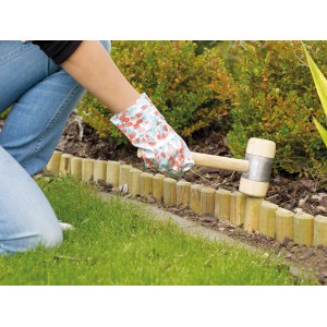 Beeteinfassung aus Holz wird mit Gummihammer im Garten verlegt.