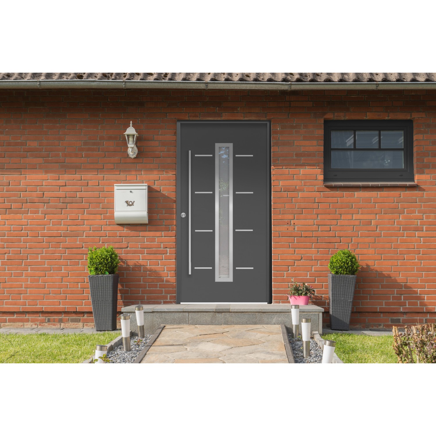Anthrazitfarbene Haustür Thermospace Milano Prime mit Glaseinsatz und Edelstahlgriff, montiert in Hausfassade.