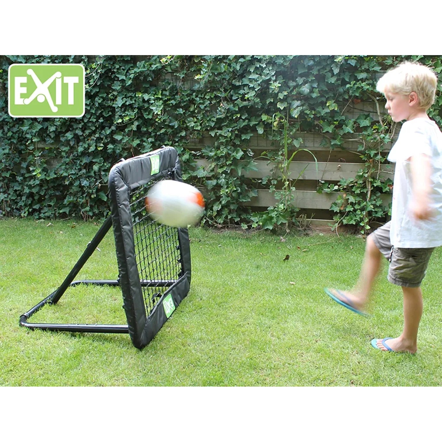 EXIT Kickback Multisport Rebounder M (84x84cm) in Aktion mit Kind beim Fußballspielen im Garten.