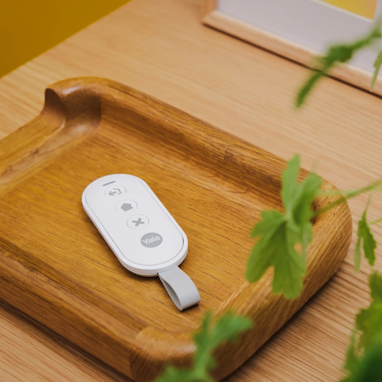 Weiße Yale Fernbedienung zur Alarmschaltung auf Holztablett. Kabellose Steuerung für Smart Alarm Systeme.