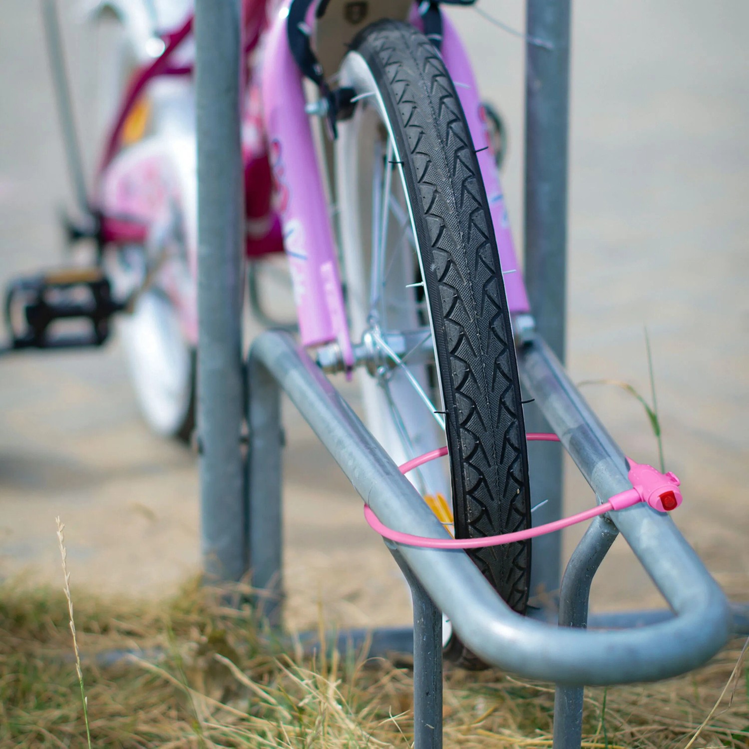 Pinkes Fahrrad mit Fahrradschloss am Fahrradständer. Kabelschloss mit Schlüssel.