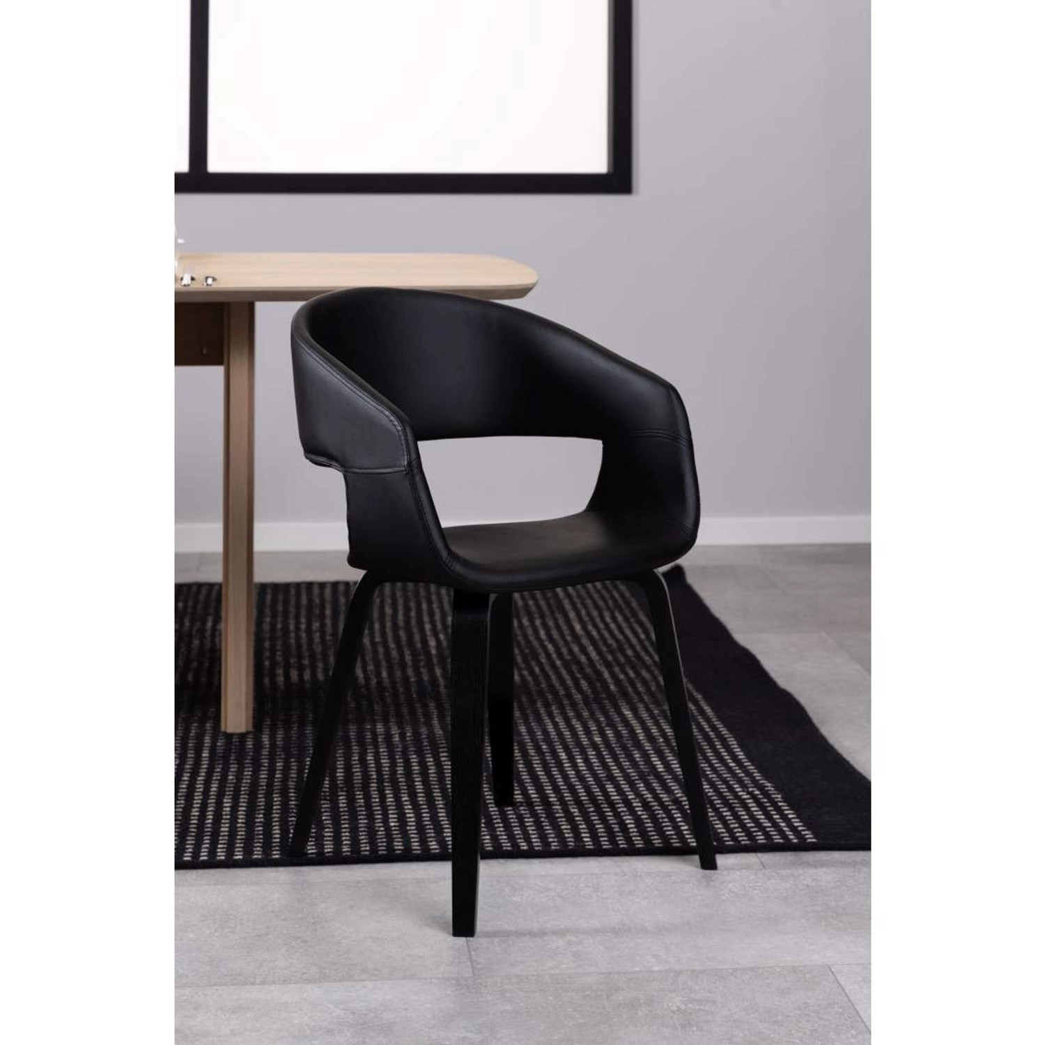 Schwarzer ebuy24 Nova Esszimmerstuhl mit Armlehne aus Kunstleder vor Esstisch und Teppich.