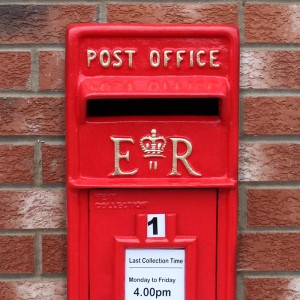 Roter Monstershop Briefkasten im englischen Stil mit "Post Office" Schriftzug an einer Backsteinwand.