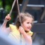 Fröhliches Mädchen schwingt an einem Wickey Spielturm mit Seil. Kinderspielplatz im Garten.