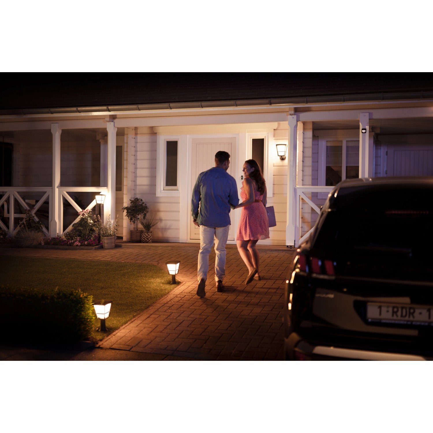 Szene mit Philips Hue Econic LED Sockelleuchten im Garten, Paar geht zum Haus.