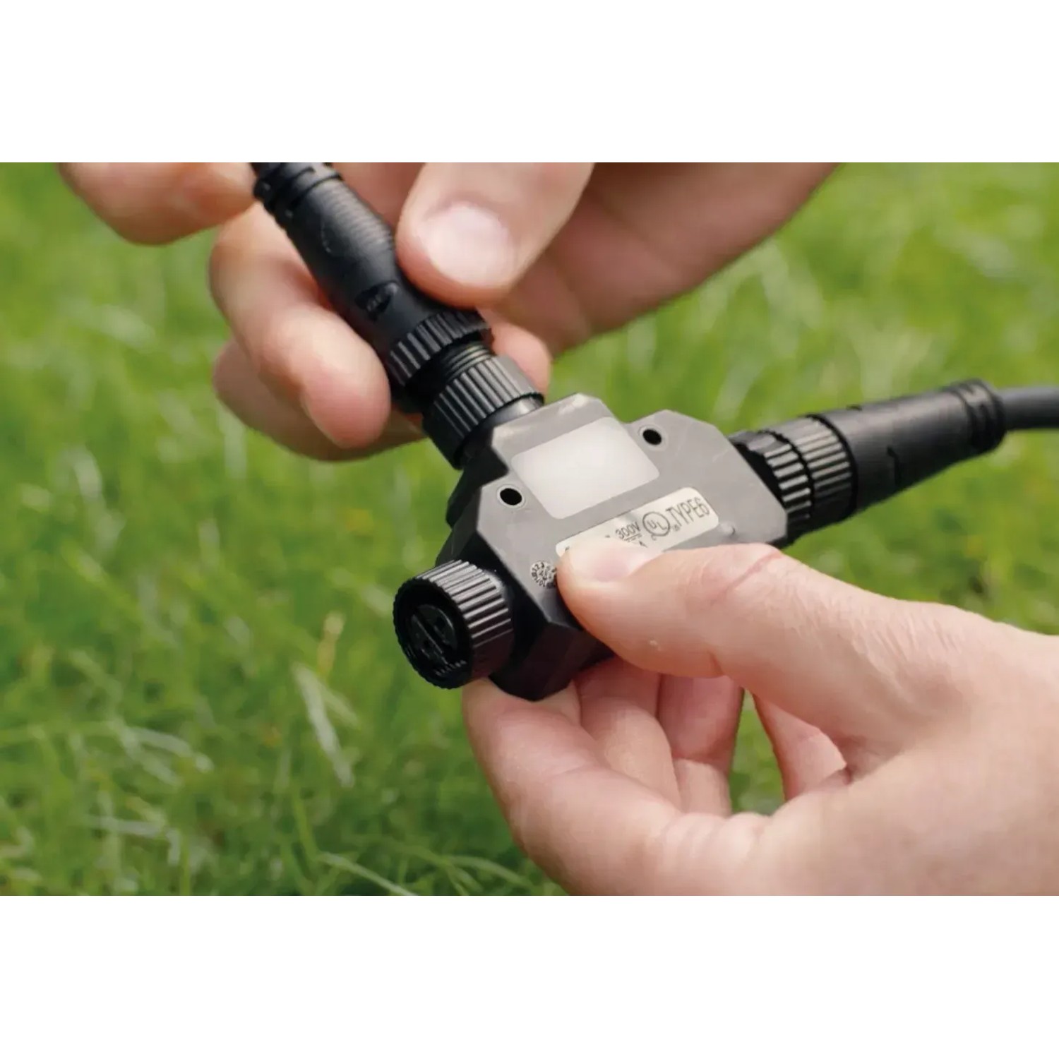 Philips Hue Outdoor T-Stecker in der Hand, Zubehör für smarte Gartenbeleuchtung.