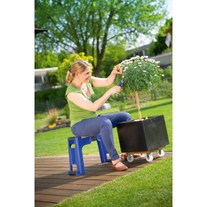 Frau sitzt auf blauem LUX Gartenhocker mit Kniekissen und schneidet Pflanze im Garten.