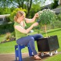 Frau sitzt auf blauem LUX Gartenhocker mit Kniekissen und schneidet Pflanze im Garten.