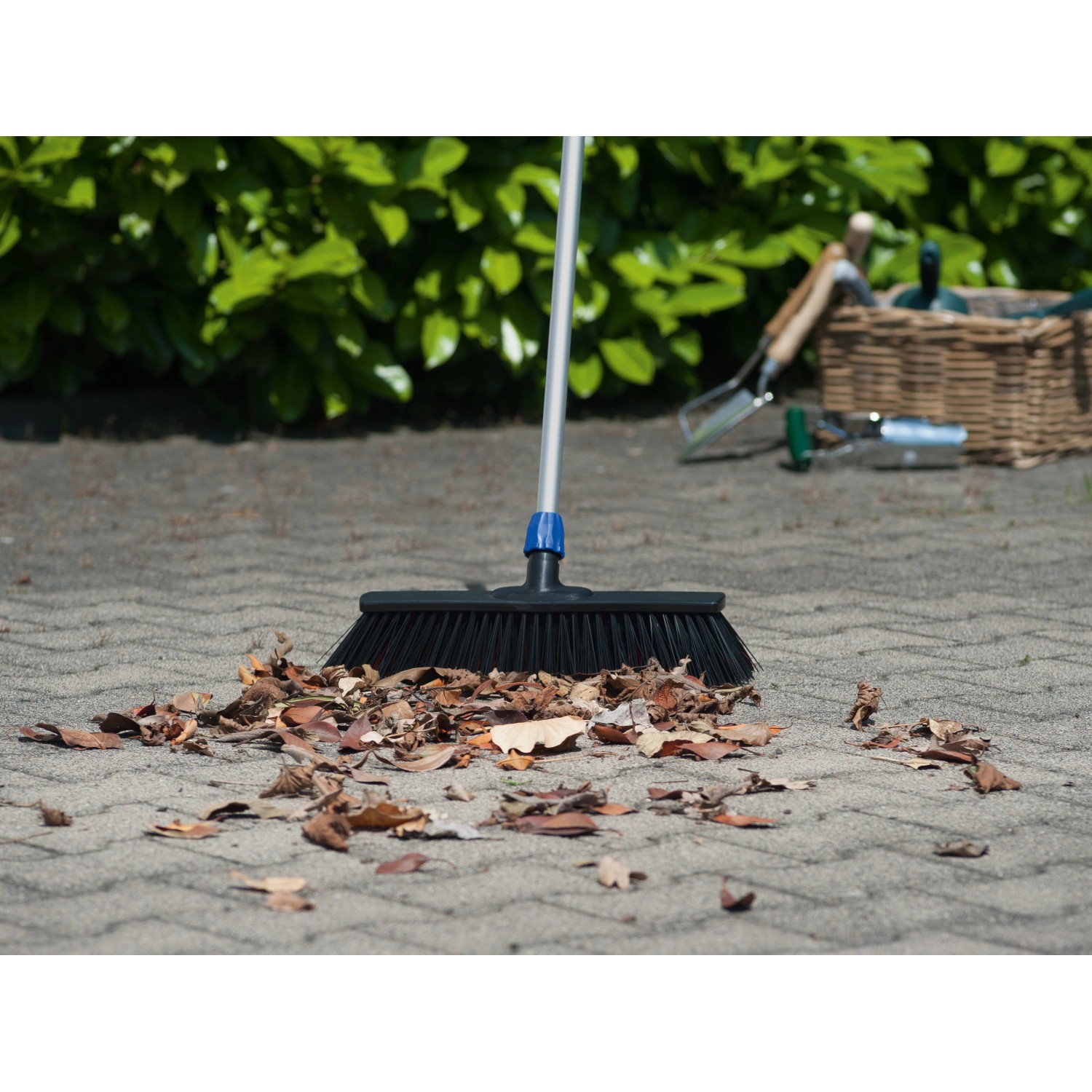 LUX Straßenbesen Professional 2in1 mit Stiel kehrt Laub auf Pflastersteinen.