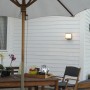Anthrazitfarbene Lutec Box Cube Außenwandleuchte an weißer Hauswand über einer Terrasse.