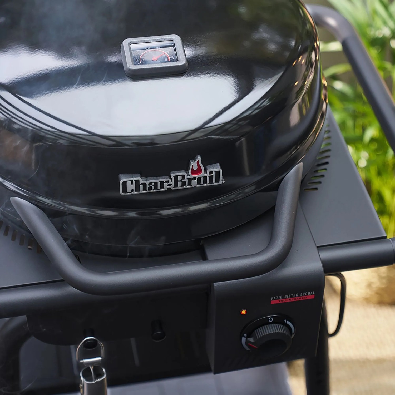 Schwarzer Char-Broil Elektrogrill Patio Bistro E2Coal mit Deckel, Thermometer und Bedienfeld. Dampf steigt auf.