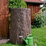 Dunkelbraune Arves Regentonne Evergreen 475 l in Baumstammoptik mit Gießkanne im Garten.