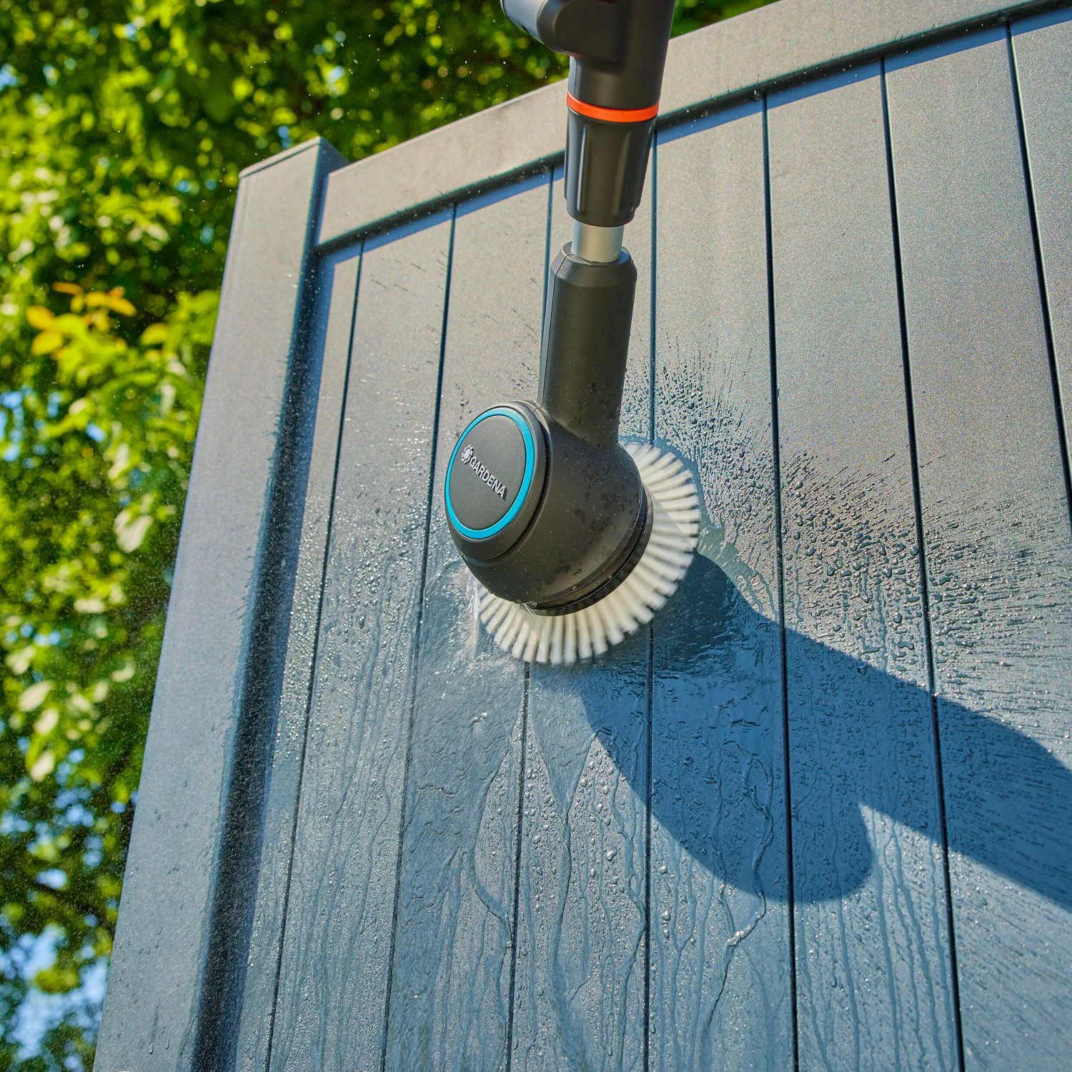 Gardena Akku-Multi-Reiniger AquaBrush Patio im Einsatz an einer grauen Holzfassade.