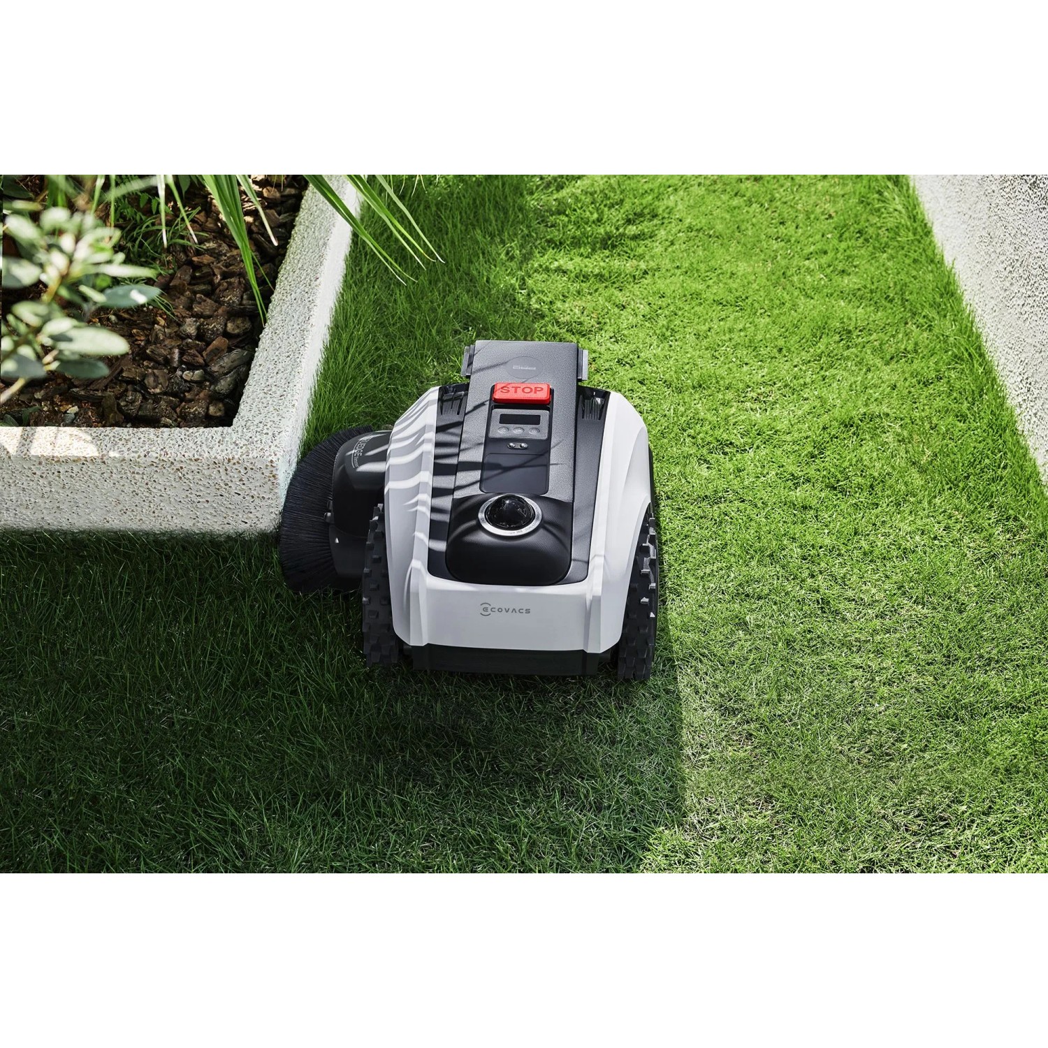 Ecovacs Mähroboter Goat O1200 in Weiß-Schwarz auf Rasenfläche, neben Beet.