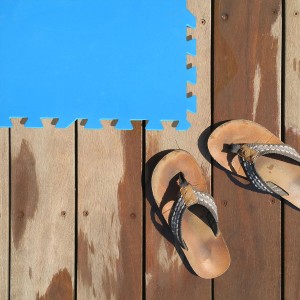Blaues eyepower Poolunterlage 36er Set (50x50 cm) neben Sandalen auf Holzdeck.