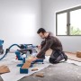 Mann schneidet Holz mit Bosch Professional Kapp- und Gehrungssäge GCM 340-305 D. Blaue Säge mit Staubabsaugung für präzise Schnitte.