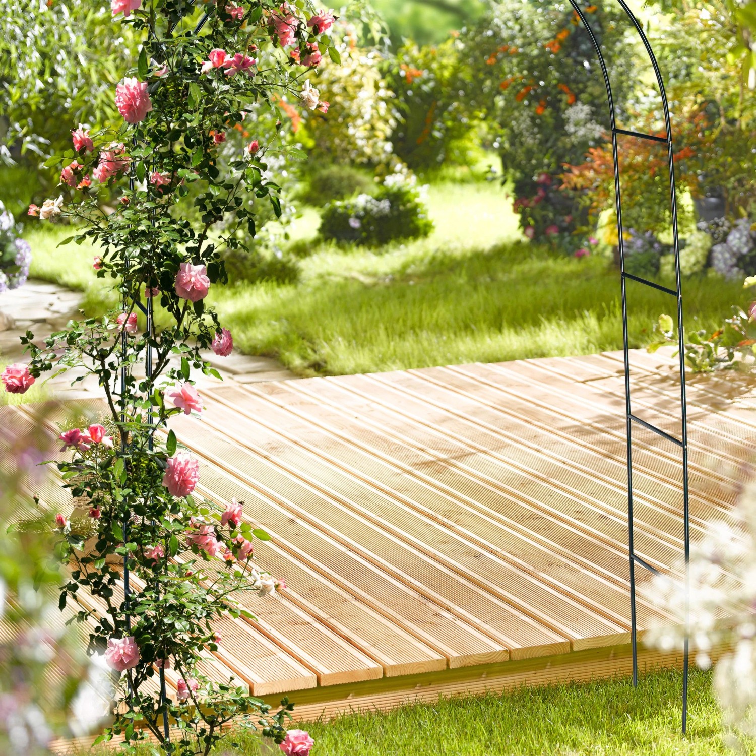 Dunkelgrüne Metall Rankhilfe mit blühenden rosa Rosen im Garten über einem Holzweg.