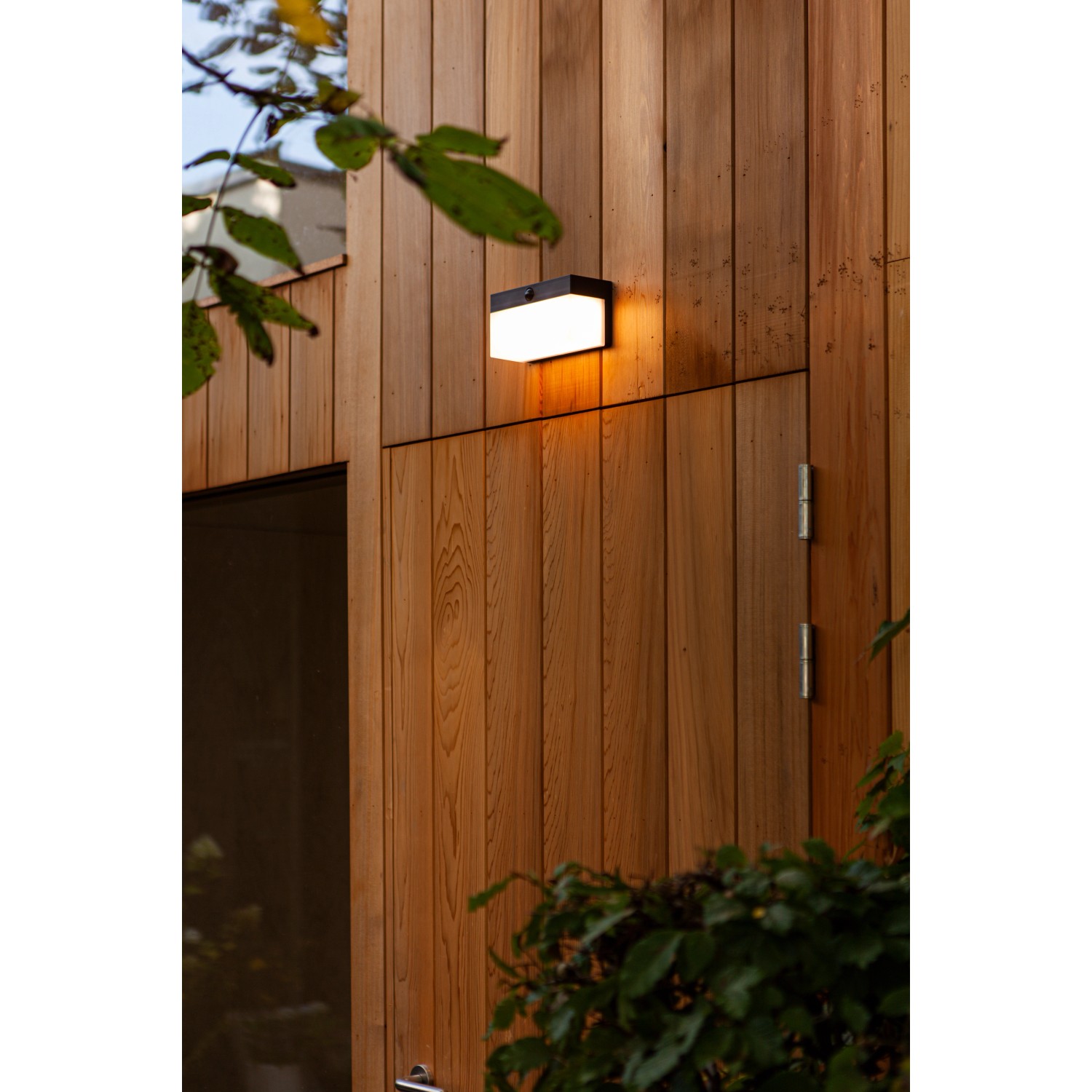 Schwarze, eckige Lutec LED Solar-Wandleuchte Fran an einer Holzwand. Mit Bewegungsmelder.