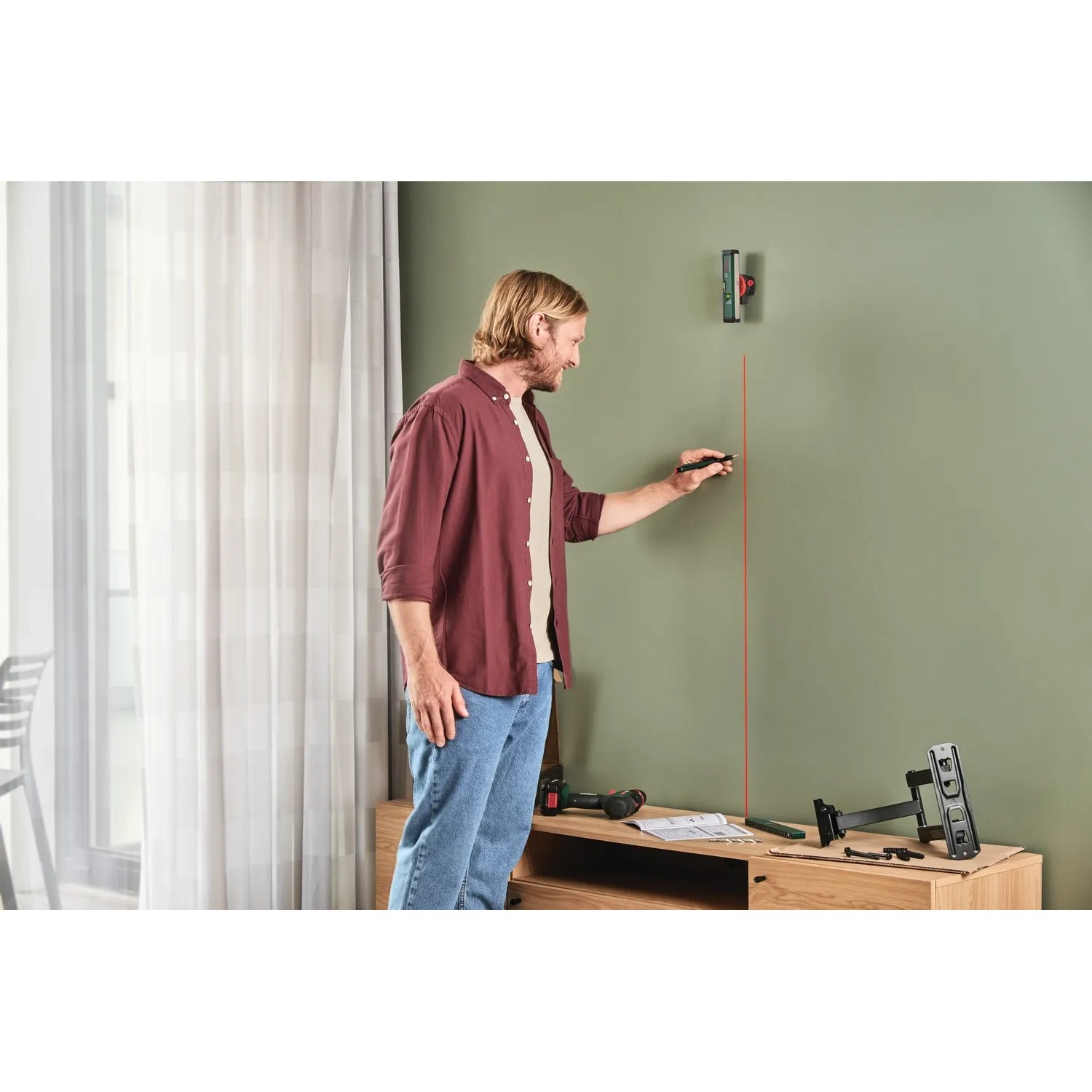 Mann benutzt Bosch UniversalWallLevel Laser-Wasserwaage zur vertikalen Ausrichtung an einer Wand.