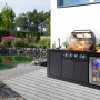 Schwarze Buschbeck Outdoorküche Liverpool mit Grill, Spüle und beleuchtetem Kühlschrank vor Gartenteich.