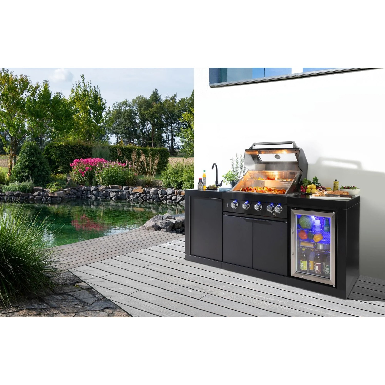 Schwarze Buschbeck Outdoorküche Liverpool mit Grill, Spüle und beleuchtetem Kühlschrank vor Gartenteich.