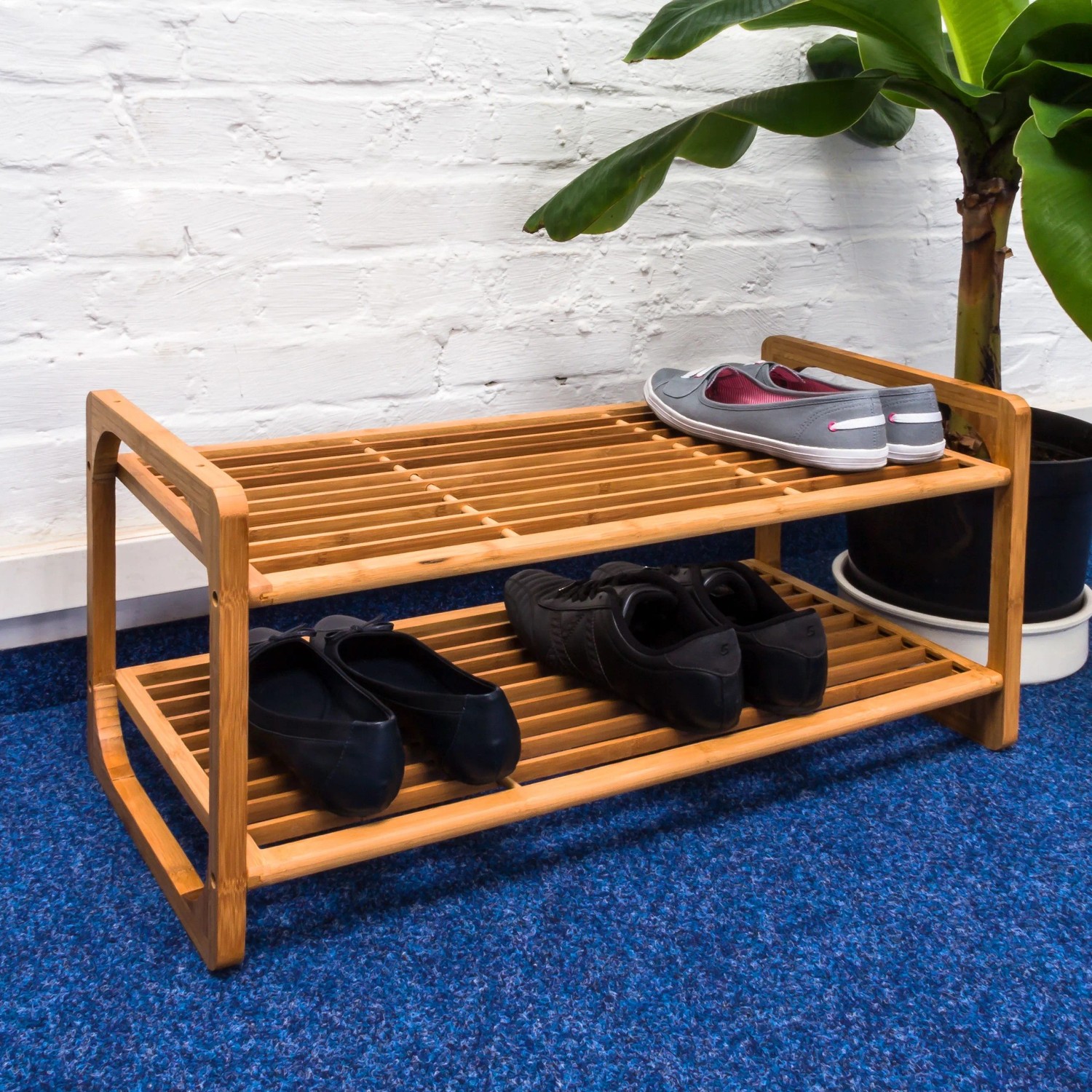 Relaxdays Schuhregal aus hellem Bambus mit 2 Ablagen, gefüllt mit Schuhen, auf blauem Teppich. Ideal für den Flur.