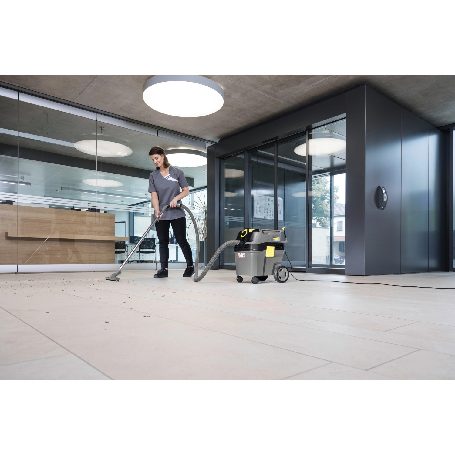 Frau nutzt Kärcher NT 30/1 Ap L Nass-/Trockensauger zur Bodenreinigung in einem Büro.