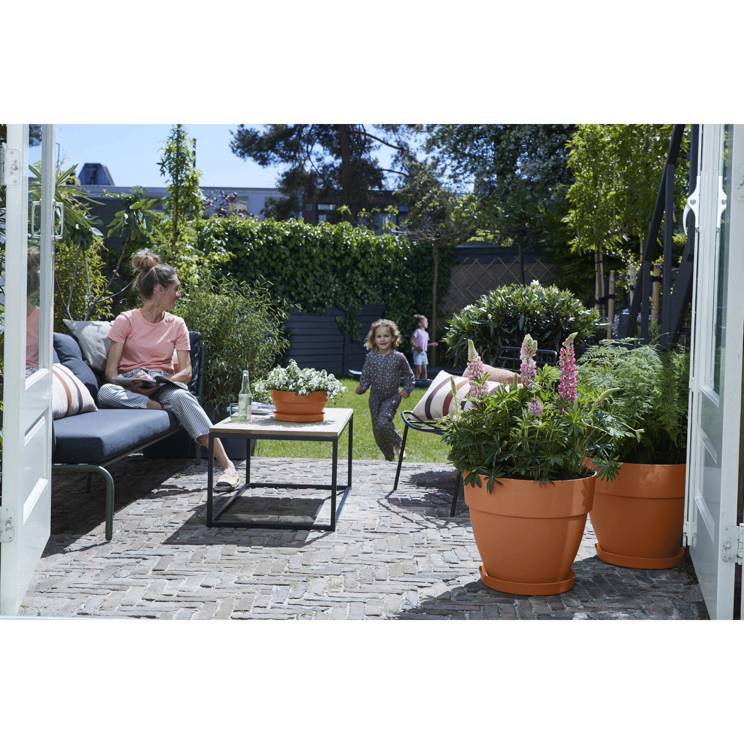 Elho Blumentopf Vibia Campana, Ø 40 cm, Terra, im Garten mit Pflanzen und spielenden Kindern.