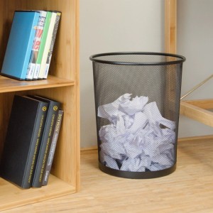 Runder schwarzer Metall-Papierkorb mit Drahtgeflecht, gefüllt mit Papier, auf Holzboden neben Regal. Ideal für Büro.