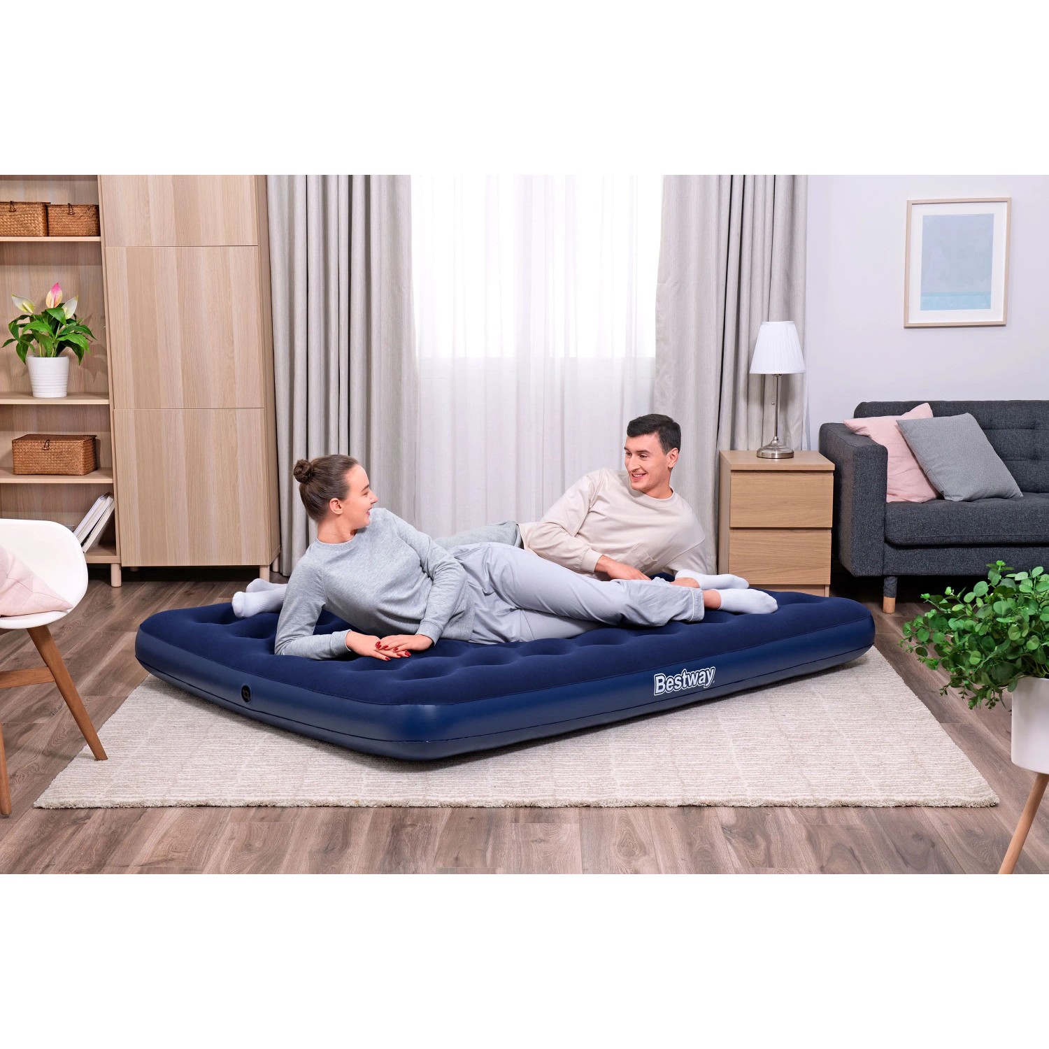 Bestway Luftmatratze Queen Size, dunkelblau, mit zwei Personen im Wohnraum.