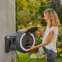 Gardena Akku-Wand-Schlauchbox PowerRoll XL mit Frau beim Akku einsetzen. Gartenschlauchwagen mit 35m Schlauch.
