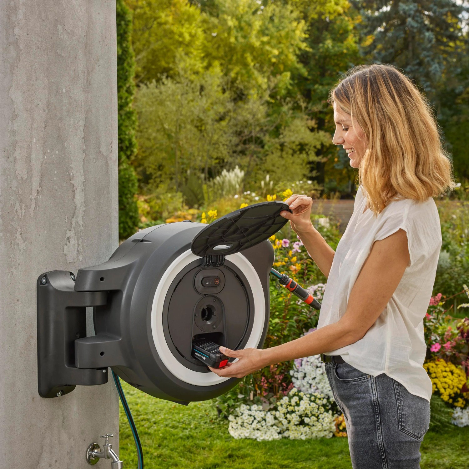 Gardena Akku-Wand-Schlauchbox PowerRoll XL mit Frau beim Akku einsetzen. Gartenschlauchwagen mit 35m Schlauch.