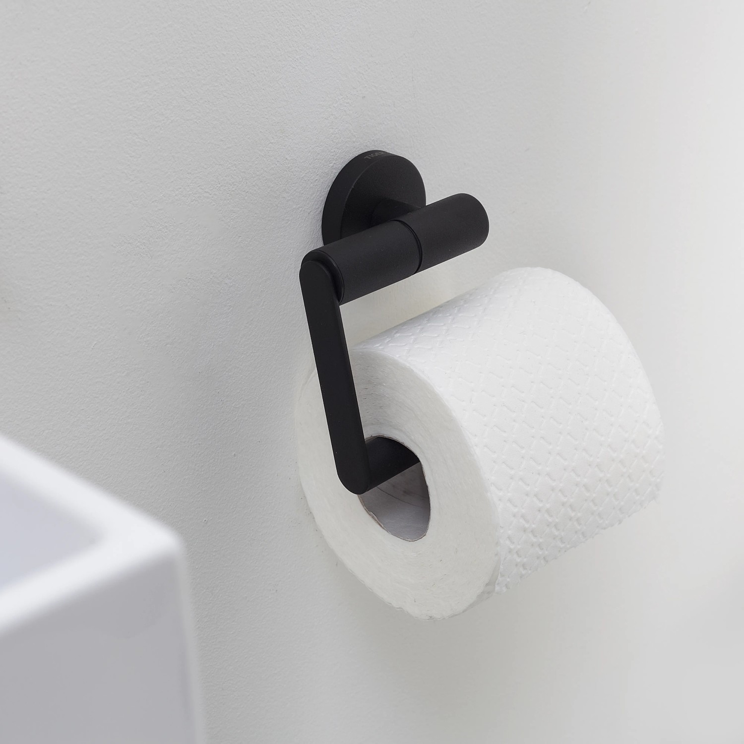 Tiger Toilettenpapierhalter Boston, Edelstahl schwarz, mit Papierrolle an weißer Wand.
