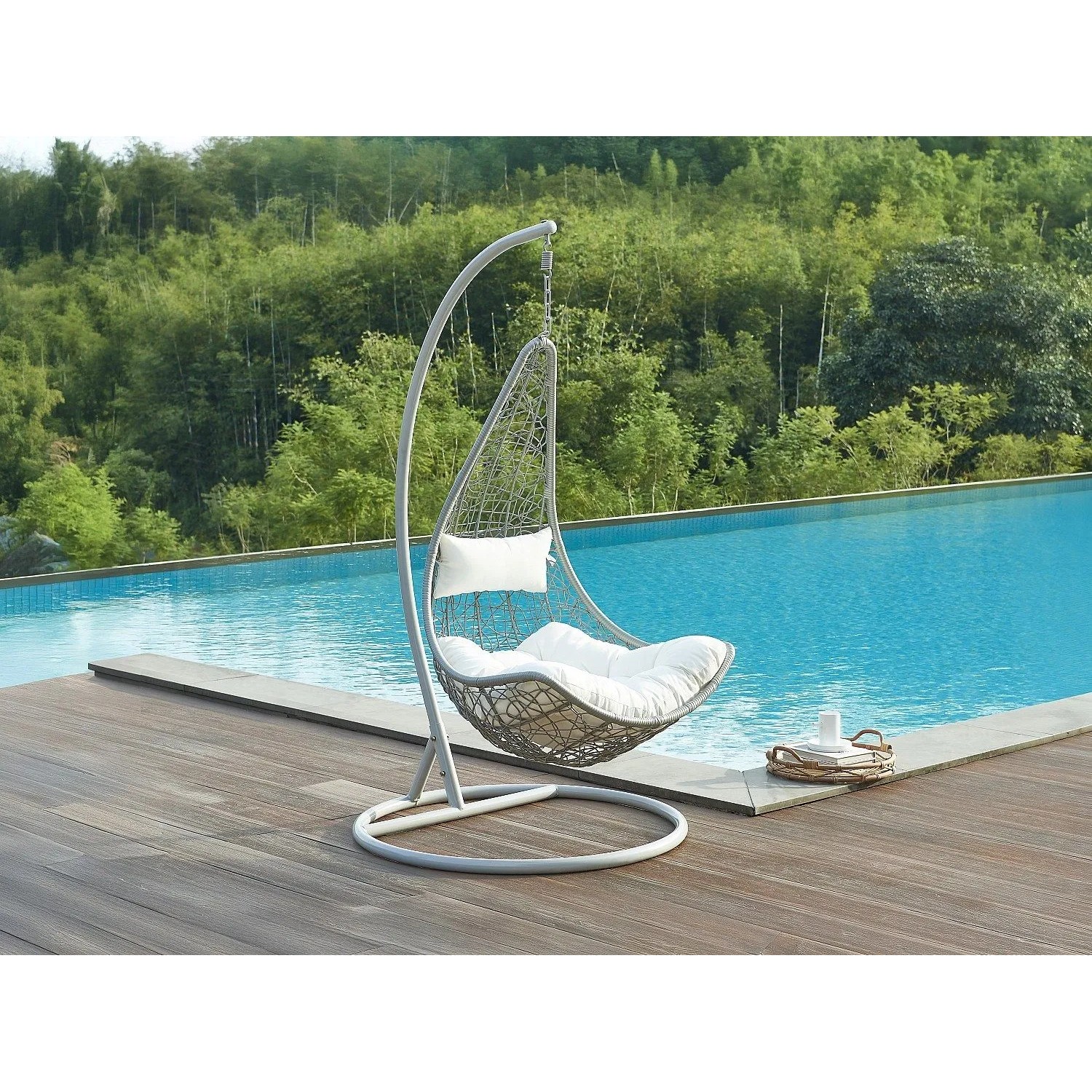 Vente-unique Hängesessel Orosi hellgrau aus Polyrattan mit weißem Kissen am Pool auf Holzdeck.
