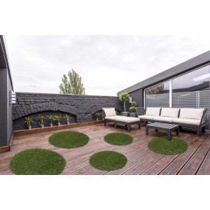 Mehrere runde, grüne Andiamo Kunstrasen-Teppiche Sansibar auf einer Holzterrasse.
