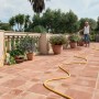 Frau bewässert Blumen mit Hozelock Expansions-Gartenschlauch SuperHoze 15m auf Terrasse.