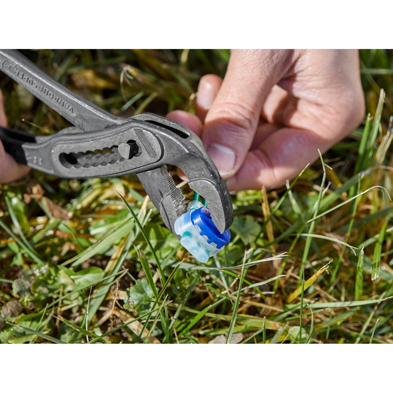 Gardena Verbinder wird mit einer Zange auf Rasen fixiert, Zubehör für Mähroboter.