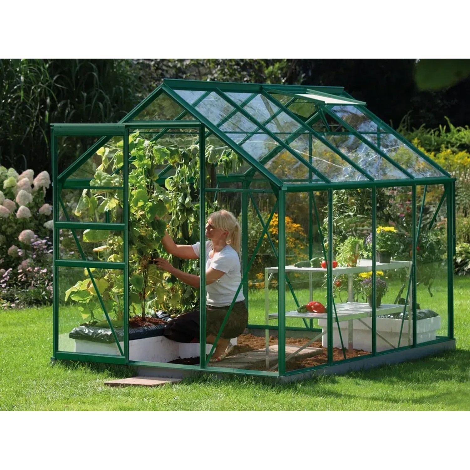 Grünes Vitavia Gewächshaus Venus 5000 mit Frau bei der Pflanzenpflege im Garten.