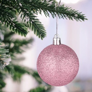 Glitzernde rosa Weihnachtskugel hängt an einem Tannenbaumzweig. Festlicher Christbaumschmuck.